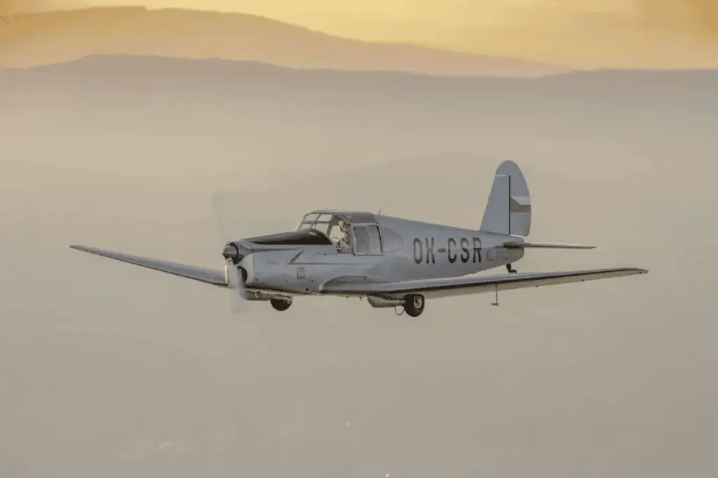M‑1 Sokol in flight Historic Czechoslovak low‑wing aircraft M‑1 Sokol in flight over landscape, black‑and‑white photograph