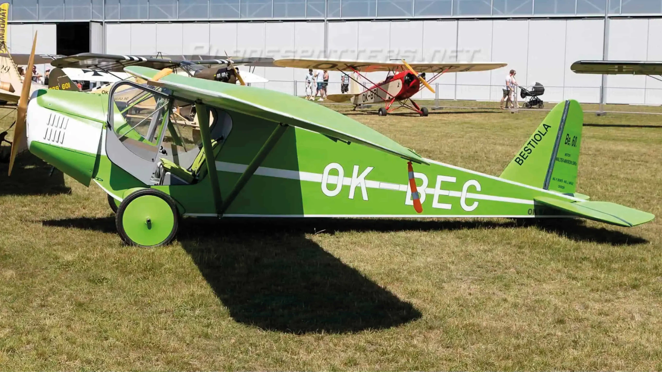 Restored Be 60 Bestiola OK‑BEC vintage Czech low‑wing aircraft in bright green livery parked on airfield during aviation exhibition