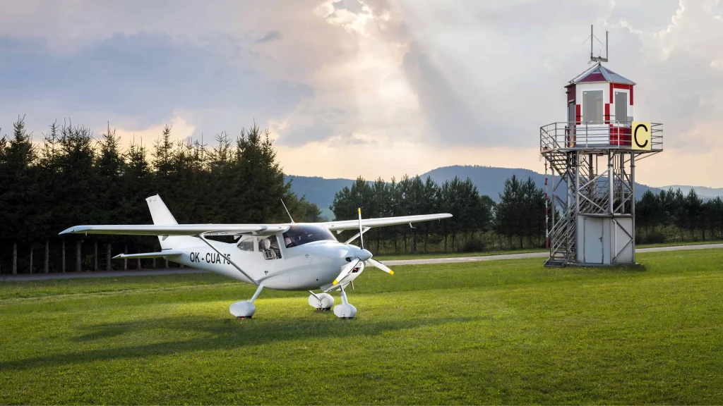 The two‑seat composite high‑wing M‑8 EAGLE on the apron, shown from the left side with its fixed nose gear and wide cabin doors visible in daylight.